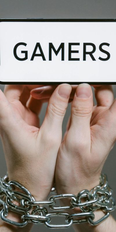 Close-up of hands bound by chains holding a phone displaying 'Gamers', symbolizing gaming addiction.