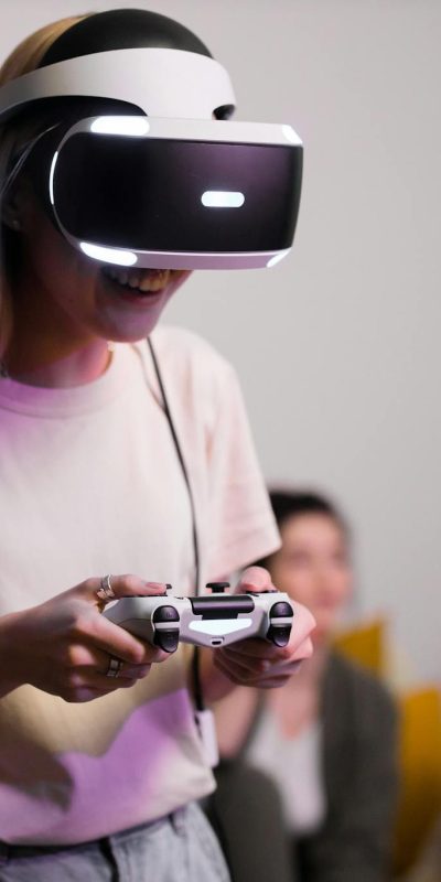Smiling woman wearing VR headset and holding a gaming controller indoors with friends.