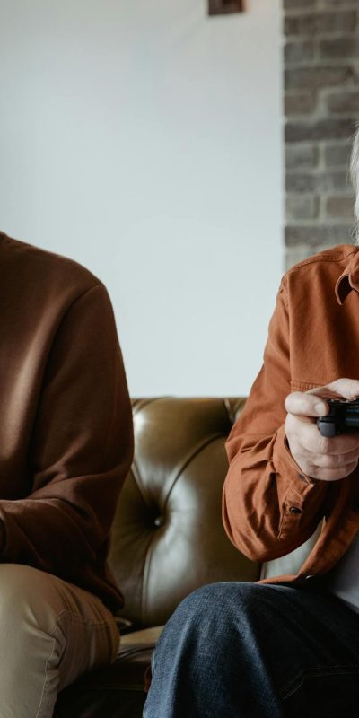 Two senior men laughing and playing video games, sharing joyful moments indoors.